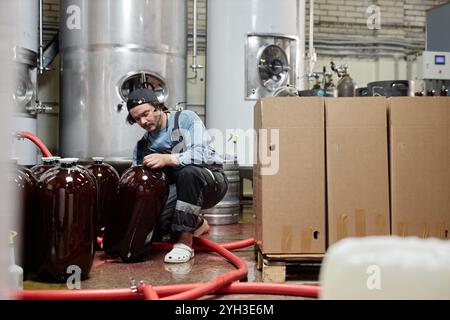 Hard working male production operator lifting huge keg of craft cider or beer packing bottles into cardboard boxes for delivering to pub from factory Stock Photo