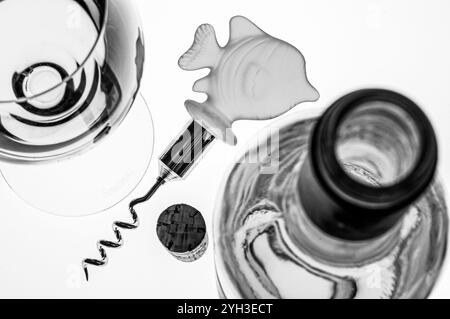 Concept fish & white wine meal food combination with white wine glass, bottle cork and fish shaped corkscrew In retro sepia black and white Stock Photo