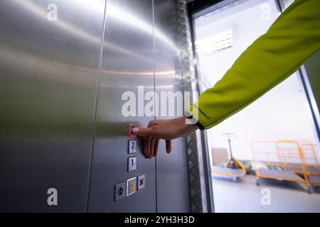 Person pressing an elevator button in a modern storage facility with visible carts. Stock Photo