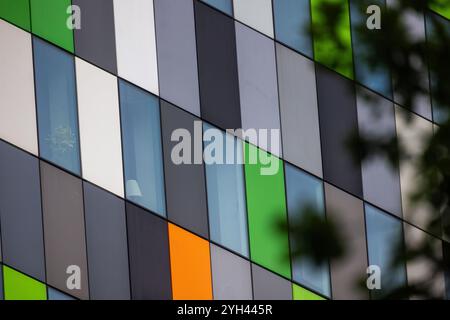 The photograph shows a modern building facade with a grid of rectangular panels in shades of green, white, orange, and grey. Some windows reveal inter Stock Photo