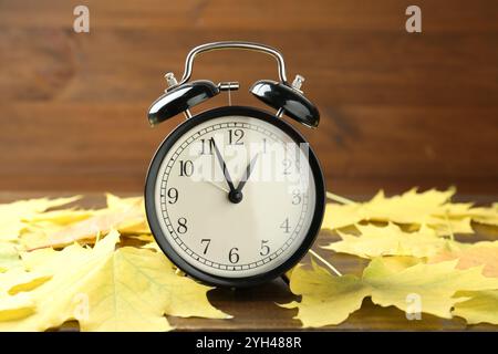 Autumn time. Alarm clock among leaves on wooden table, closeup Stock Photo
