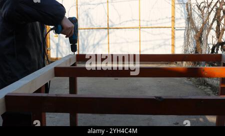 man drilling holes in wooden frame during construction of outbuilding in yard, working with building frame using hand tool in village Stock Photo