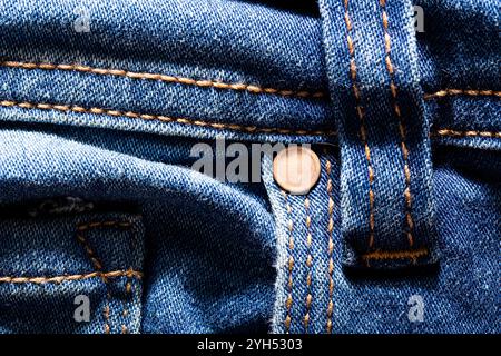 A closeup shot of blue denim fabric with a single button and intricate stitching. The texture of the fabric is visible, highlighting the weave and thr Stock Photo