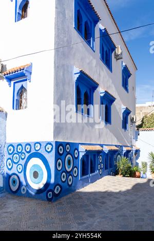 A white painted building with blue colored windows,  part of the wall painted with blue circles at medina in Chefchaouen, Morocco. Stock Photo