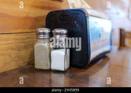 Salt and Pepper shakers next to a napkin dispenser on a wooden cafe table. Stock Photo