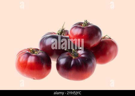 Close-up view of ripe heirloom tomatoes with deep red and purple hues, isolated on pale pink background. Stock Photo