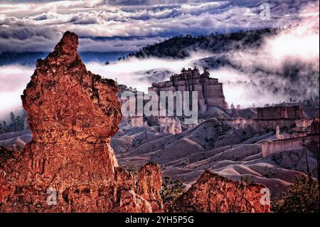 Low clouds drift through Bryce Canyon National Park, Utah, creating a misty, ethereal atmosphere that softens the rugged red rock formations. Stock Photo