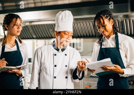 Professional Asian senior chef guides diverse students in a restaurant kitchen workshop. Focusing on Stock Photo