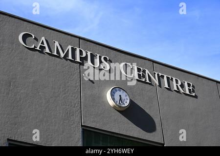 Campus Centre sign on a grey wall, above an analogue clock, at Monash University during a sunny day Stock Photo