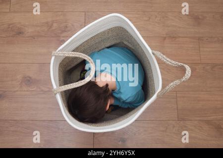 A sorrowful toddler baby hides alone in the basket, seeking a feeling of safety from his fears. The frightened child is curled up inside the basket, h Stock Photo