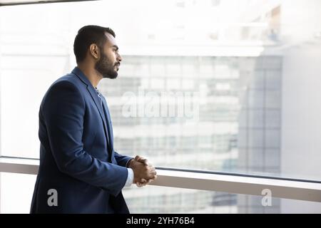 Pensive young Indian businessman standing at window Stock Photo