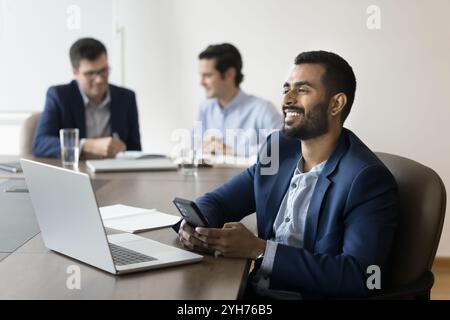 Successful dreamy young Indian office professional man using digital devices Stock Photo