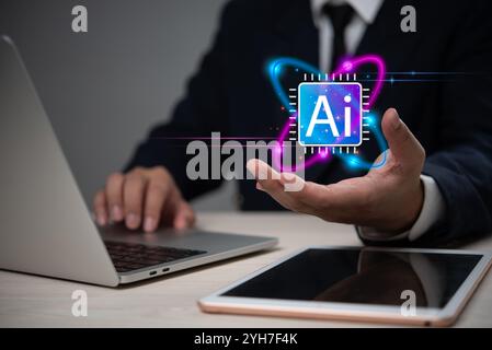 Businessman presenting a glowing AI icon above his hand, with a laptop and tablet on the desk, representing artificial intelligence technology. Stock Photo