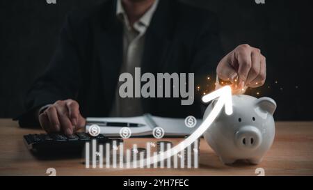 Businessman placing coin into a piggy bank with rising financial chart overlay, savings, investment growth, and financial planning. economic success a Stock Photo