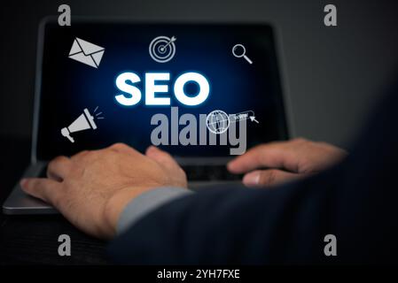Hands typing on a laptop displaying SEO with digital marketing icons. Enhances understanding of SEO strategy and digital marketing techniques. Ideal f Stock Photo