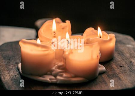 Wax candles burning on a wooden board or table, cozy atmosphere, warm and dark background, close up Stock Photo