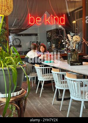 A scene in the popular cafe / restaurant A.Horn in Kreuzberg, Berlin, Germany, a neon sign saying 'be kind' in the background Stock Photo