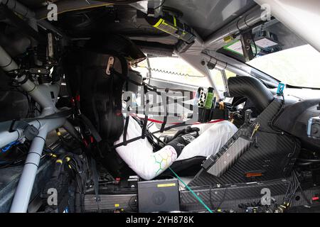 Race car driver wearing helmet and safety gear sits in car, preparing for race, holding steering wheel Stock Photo