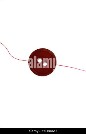 Still life of a single red button and a strand of red thread on a white background Stock Photo