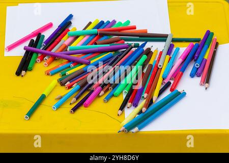 Multi-colored pencils, felt-tip pens, sheets of white paper on the table. Preschool education Stock Photo