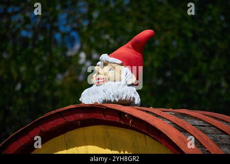 The head of a gnome with a white beard and a red hat sitting on a wooden barrel. Stock Photo