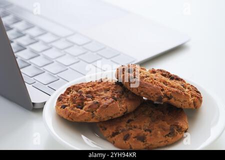Chocolate chip cookies on a plate near a laptop. Close up. Stock Photo