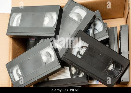 A box filled with a large number of black VHS tapes. The tapes are old and worn, and they are stacked on top of each other in the box Stock Photo