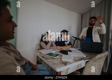 High school students collaborating on a school project with their professor in a cozy home setting, surrounded by notebooks and a laptop. Stock Photo