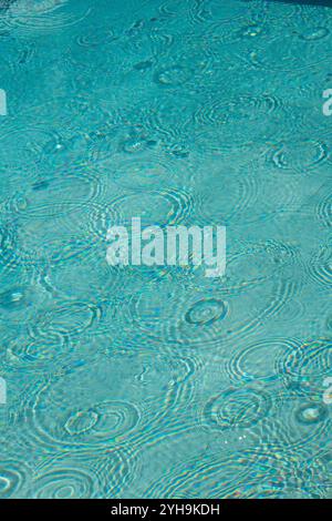 abstract image of raindrops falling on the surface of a swimming pool causing ripples and a pattern on the water's surface suitable for background Stock Photo