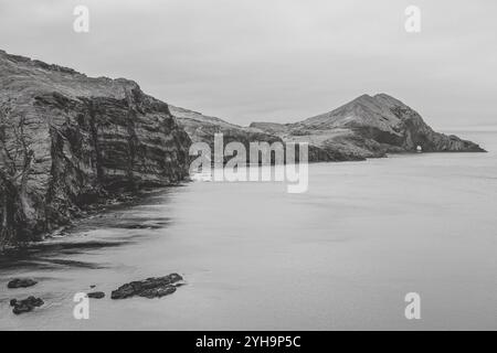 Sao Lourenco, Madeira - A dramatic black and white landscape with rugged cliffs and a calm sea, featuring a natural rock arch. Stock Photo