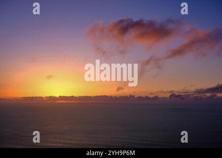 A breathtaking view of the ocean during a colorful sunset. The horizon is highlighted by soft, warm hues as the sun sinks below the clouds. Stock Photo