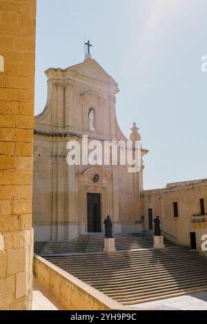 Cittadella, Gozo - View of a historic church with statues standing at the entrance and grand stairs leading up to the building under the bright sky. Stock Photo