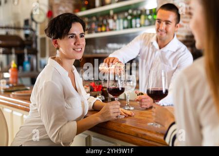 Two girlfriends chat with each other and drink red wine while sitting at bar in restaurant Stock Photo