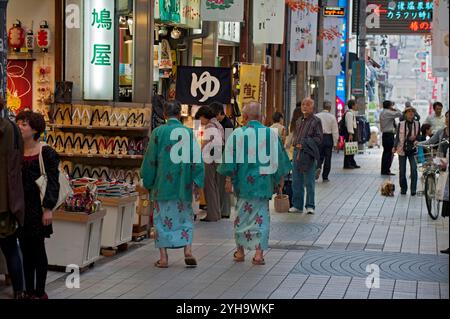 Visitors wearing traditional yukata robes walking along a shopping arcade in the hot spring spa resort town of Dogo Onsen, Matsuyama, Ehime, Japan. Stock Photo