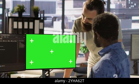 System administrator does software debugging on isolated screen PC, asking for help from coworker. Zoom in on admin fixing coding mistakes on chroma key computer, being assisted by colleague, camera A Stock Photo
