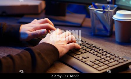 Hacker in secret underground shelter typing on keyboard, writing lines of code on computer, trying to get past security systems with virus. Scammer working on hacking script, camera B close up shot Stock Photo