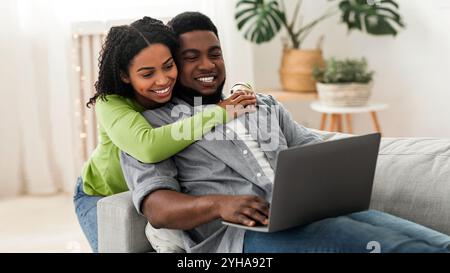 Cheerful black couple web surfing on laptop at home together Stock Photo