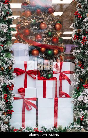 Gift boxes in store window. Season of Christmas shopping and sales. White boxes with red ribbons on background of Christmas decorations. Stock Photo