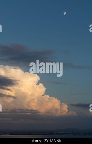 Big clouds at sunset, the moon in a blue sky and the river. Nature and city landscape at the end of the day with beautiful light, calm background Stock Photo