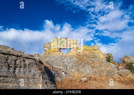 Weathered sandstone cliff with monster-like silhouette, covered in yellow-green lichen against vivid blue sky. Popular 'Monster Rock' photo spot at Is Stock Photo