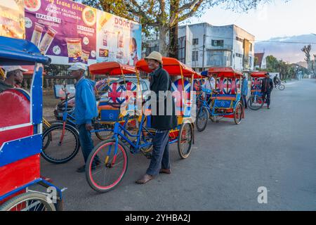 Antsirabe, Madagascar - August 30, 2024: A row of colorful rickshaws waiting for tourists near the old train station. The vibrant rickshaws are a popu Stock Photo