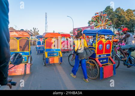 Antsirabe, Madagascar - August 30, 2024: Colorful traditional rickshaws line up near the Ferris wheel in this highland city. These rickshaws are a pop Stock Photo