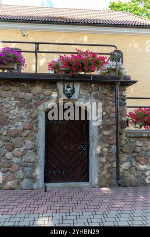A rustic wooden door is set in a stone wall with colorful flowers hanging above it. Stock Photo