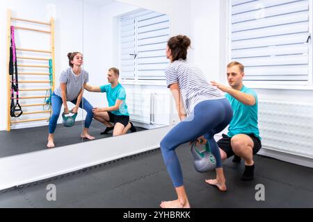 Woman with lower back pain in physical therapy. Physical therapist exercising with female patient doing back mobility exercises using a kettlebell. Stock Photo