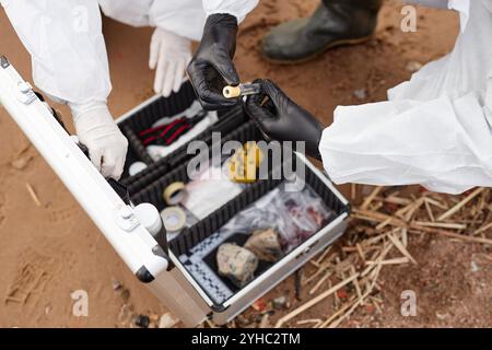 Top view closeup of two unrecognizable scientists wearing hazmat suits and holding test tube with water in gloved hands while doing probes outdoors, copy space Stock Photo