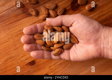 Close up of hand holding fresh organic almonds on rustic wooden surface, healthy eating concept Stock Photo