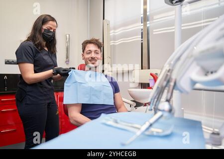 latina woman dentist putting a bib on a smiling man sitting in the chair to perform a procedure Stock Photo