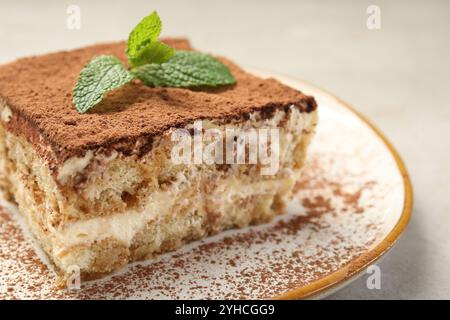 Piece of tasty tiramisu with fresh mint on beige table, closeup Stock Photo