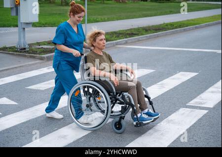 Red-haired nurse pushing an elderly woman in a wheelchair across the ...