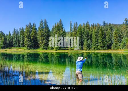 Eagle County Emerald Lake with coniferous trees and mirror sky reflection on water surface and man fishing with rod and reel inside Stock Photo